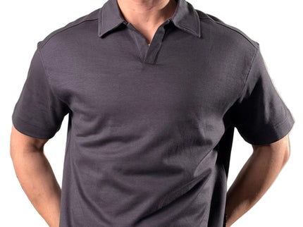 Man wearing a dark gray polo shirt standing indoors with a plant and black couch in the background.